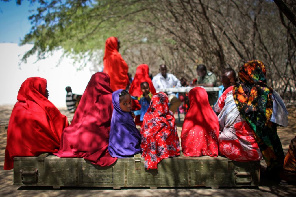 African villagers wearing red clothing sitting under a tree to shade from the sun